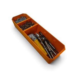 Op de afbeelding: Een oranje kunststof opbergbak met drie aparte vakken. De twee kleinere vakken bevatten zilver- en goudkleurige metalen schroeven, terwijl het grootste vak een gereedschap met een geel handvat en diverse metalen boortjes bevat.