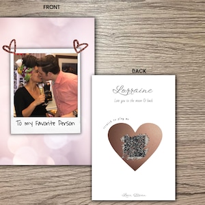 May include: A white card with a pink and white background. The front of the card has a photo of a couple kissing. The photo is in a white frame with a red heart on each side. The text "To my Favorite Person" is written below the photo. The back of the card has a rose gold heart with a scratch-off surface. The text "Lorraine Love you to the moon & back" is written above the heart. The text "Love, Brian" is written below the heart.