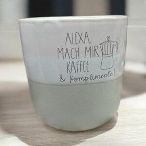 Puede incluir: Una taza de cerámica azul claro y blanco con el texto "Alexa, mach mir Kaffee & Komplimente!" y un dibujo de una cafetera.