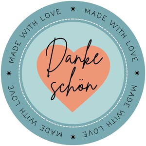 Pu&ograve; includere: Un cerchio blu chiaro con un bordo bianco tratteggiato e un cuore color pesca al centro. Il cuore ha testo nero che dice "Danke sch&ouml;n" e il cerchio ha testo nero che dice "Made with love" ripetuto quattro volte.