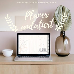 Könnte beinhalten: Ein Laptop mit weißem Hintergrund auf dem Bildschirm. Der Bildschirm zeigt einen digitalen Planer mit den Worten "JOURNAL" und einer einfachen Linienzeichnung einer Pflanze. Der Laptop steht auf einem Holztisch mit einer weißen Schüssel und einer Vase mit einem getrockneten Palmblatt.