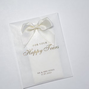 Pu&ograve; includere: Busta in carta velina bianca con un fiocco di raso bianco e scritta dorata che recita "For Your Happy Tears" e "Mr. & Mrs. Jones 17.07.2023".