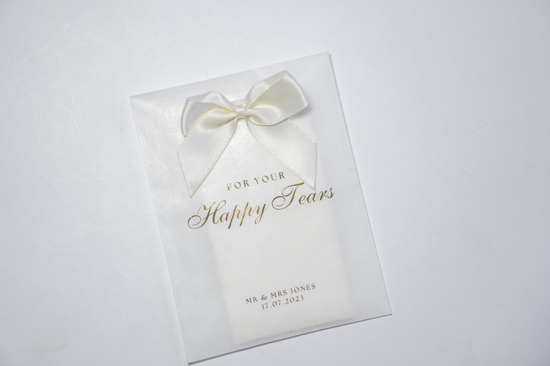 Pu&ograve; includere: Busta in carta velina bianca con un fiocco di raso bianco e scritta dorata che recita "For Your Happy Tears" e "Mr. & Mrs. Jones 17.07.2023".