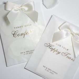 Pu&ograve; includere: Due sacchetti di carta bianchi con lettere dorate e fiocchi di raso bianco. Un sacchetto dice "Throw some confetti" e l'altro dice "For your happy tears". Entrambi i sacchetti hanno il testo "MR & MRS JONES 17.07.2023".