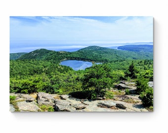 May include: A panoramic view from a mountaintop overlooking a small, heart-shaped lake surrounded by lush green trees. The ocean is visible in the distance, with a hazy blue sky above.