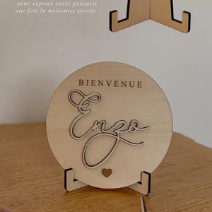 May include: Wooden welcome sign with the name "Enzo" in cursive script, a heart, and the word "Bienvenue". The sign is displayed on a wooden stand. The image also shows a separate stand.