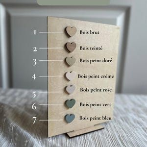 May include: A wooden display board with seven heart-shaped wood samples in various colors. The text "Choix du bois" is at the top. The samples include raw wood, stained wood, gold, cream, pink, green, and blue.