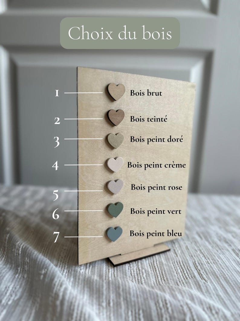 May include: A wooden display board with seven heart-shaped wood samples in various colors. The text "Choix du bois" is at the top. The samples include raw wood, stained wood, gold, cream, pink, green, and blue.