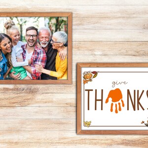 May include: A framed photograph of a family of four smiling and laughing together. The photo is in a brown wooden frame. Below the photo is a framed print with the words "give THANKS" in brown lettering with an orange handprint in the middle. The print is also in a brown wooden frame.