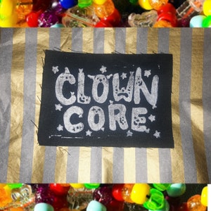 Op de afbeelding: Zwarte stoffen patch met witte tekst die "CLOWN CORE" luidt in een gestileerd lettertype. De tekst is omringd door witte sterren.