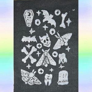 Può includere: Toppa in tessuto nero con un design bianco di vari motivi inquietanti di Halloween, tra cui pipistrelli, teschi, falene, denti, ossa e lapidi.