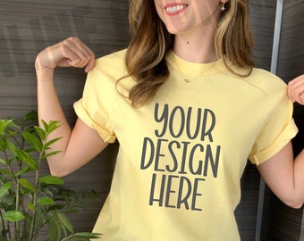 Könnte beinhalten: Eine Frau trägt ein gelbes T-Shirt mit dem Aufdruck "YOUR DESIGN HERE". Sie trägt eine blaue Jeans und sitzt.