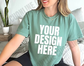 May include: A woman wearing a green t-shirt with the text "YOUR DESIGN HERE" in white. The t-shirt is a relaxed fit and has a crew neck.