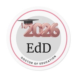 May include: A round sticker with a pink border and a gray center. The sticker features the rose gold numbers "2026" with a graduation cap on top. Below the numbers is the text "EdD" and "DOCTOR OF EDUCATION".