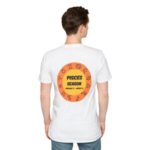 May include: White t-shirt with a circular design on the back. The design features a yellow circle with the words "PISCES SEASON" and "FEBRUARY 19 - MARCH 20" in black text. The circle is surrounded by orange zodiac symbols.
