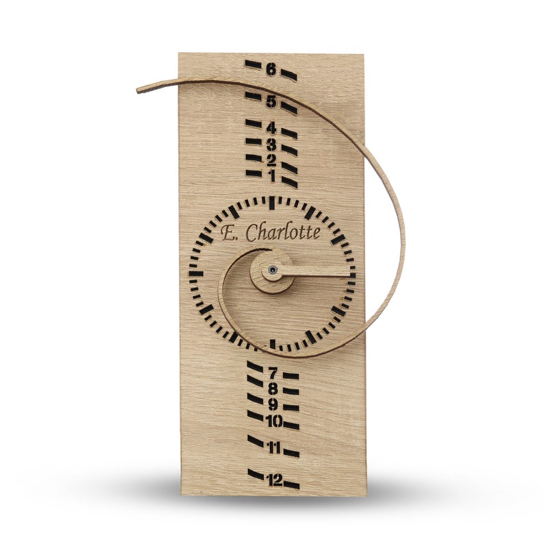 May include: Wooden clock with a spiral design and a personalized name, "E. Charlotte", on the face. The clock has numbers 1 through 12 on the outer edge and a small knob for setting the time.
