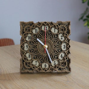 May include: A wooden clock with a black face and intricate laser-cut design. The clock has Roman numeral hour markers and a white minute hand and red hour hand.