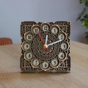 Puede incluir: Un reloj de madera con un diseño de mandala decorativo. La esfera del reloj tiene números romanos y una aguja de hora roja y una aguja de minutos blanca.