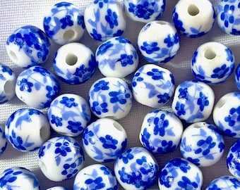 Puede incluir: Una colección de cuentas de cerámica azul y blanca con un patrón floral. Las cuentas son redondas y tienen un acabado brillante.