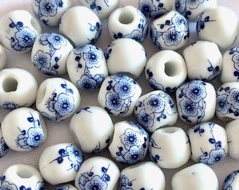 Puede incluir: Un conjunto de cuentas de cerámica blanca con un diseño floral azul. Las cuentas son redondas con un agujero en el centro, y el diseño azul presenta delicadas flores y hojas. Ideales para la creación de joyas.