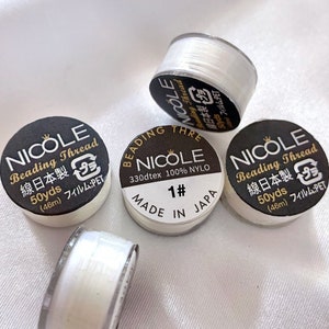 May include: Four spools of white beading thread, each with a black label that reads "Nicole Beading Thread" and includes details like "330dtex 100% NYLO", "Made in Japan", and "50yds (46m) Film: PET".