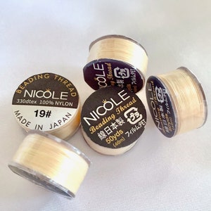 May include: Four spools of beige nylon beading thread. Each spool has a black label with the brand name "Nicole" and the text "Beading Thread" in Japanese and English. The label also includes the size "50yds (46m)" and the material "Film: PET".