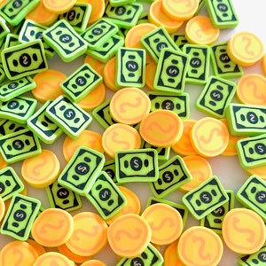 Peut inclure: Une collection de breloques en plastique représentant de l'argent et des pièces de monnaie, de couleur verte et jaune. Les breloques ont la forme de billets de banque et de pièces de monnaie avec un signe dollar dessus.