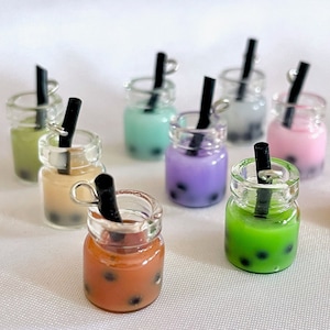 May include: Assortment of eight miniature glass jars with black straws and colourful bubble tea inside. The jars are clear and have a silver charm attached to the top.