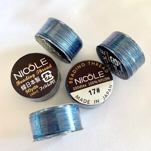 以下が含まれることがあります： 青いビーズ糸の糸巻きが4つあり、それぞれに「Nicole Beading Thread 330dtex 100% Nylon 17# Made in Japan」と書かれたラベルが付いています。