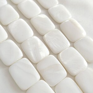 May include: A close-up shot of a string of white, rectangular beads. The beads have a smooth, glossy finish and are strung together. The beads are a bright, opaque white colour. These beads are likely for jewellery making.
