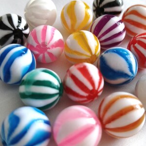 May include: A collection of round, spherical beads featuring a white base with vibrant, swirling stripes in various colours including blue, green, pink, yellow, orange, red, purple, and black. Each bead has a smooth, glossy finish and a central hole.