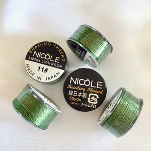 May include: Four spools of green beading thread, each with a black label. The label reads "Nicole Beading Thread 330dtex 100% Nylon 11# Made in Japan" and "Nicole Beading Thread 線日本製 50yds (46m) フィルム:PET".