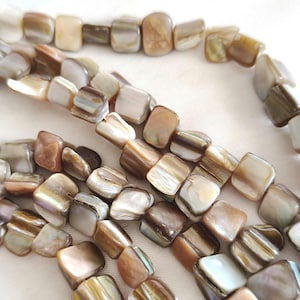 Puede incluir: Primer plano de hileras de cuentas cuadradas en tonos marrón, beige y crema. Las cuentas tienen un brillo nacarado, con variaciones de color y textura. Las cuentas están ensartadas, para un collar o pulsera.