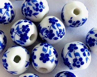 Puede incluir: Una colección de cuentas de cerámica blanca con diseños florales azules. Las cuentas tienen un agujero en el centro para enhebrar.