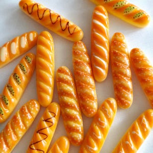 Puede incluir: Una colección de dijes en miniatura con forma de baguette en tonos marrón dorado. Algunos presentan detalles blancos moteados, otros tienen líneas en zigzag de color marrón oscuro y algunos tienen patrones moteados verdes, todos con un acabado brillante.