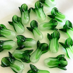 May include: A collection of 17 green and white glass bok choy charms. The charms are made of glass and have a realistic bok choy shape.