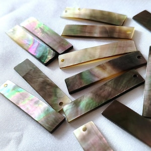 Può includere: Una collezione di componenti rettangolari in madreperla, ognuno caratterizzato da una superficie iridescente con sfumature vorticose di verde, rosa e marrone. Molti di questi pezzi piatti e allungati presentano un piccolo foro circolare vicino a un'estremità.