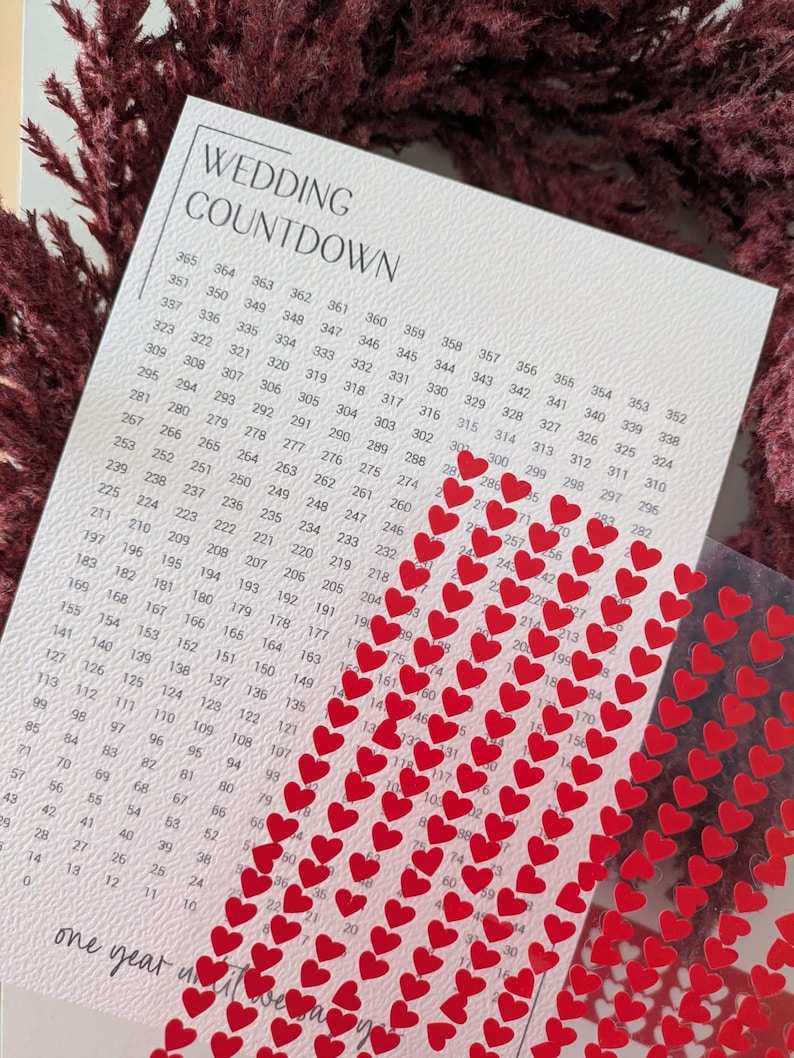 May include: A wedding countdown calendar with a white background and a grid of numbers. Red heart stickers are placed on the calendar. The text "WEDDING COUNTDOWN" is at the top.