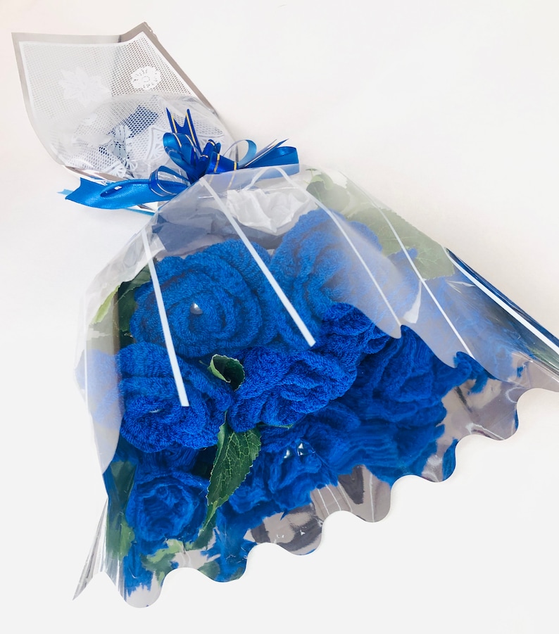 Puede incluir: Un ramo de rosas azules de toalla, envuelto en celof&aacute;n transparente. El ramo est&aacute; atado con una cinta azul e incluye hojas verdes. El celof&aacute;n est&aacute; decorado con un patr&oacute;n blanco similar al encaje.