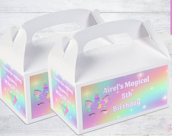 May include: Two white favor boxes with unicorn designs and rainbow backgrounds. The boxes have handles and are decorated with the text "Thanks for making my party magical" and "Airel's Magical 5th Birthday".
