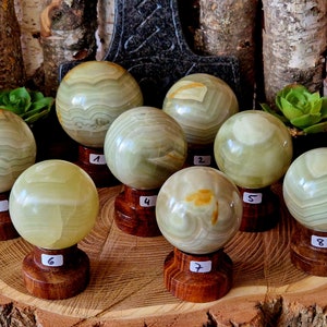 Puede incluir: Ocho esferas de ónix verde y amarillo en soportes de madera. Las esferas están pulidas y tienen un patrón en capas. Los soportes están numerados del 1 al 8.