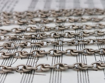 May include: Multiple strands of silver chain, laid out on a sheet of music. The chain has a delicate, twisted design.