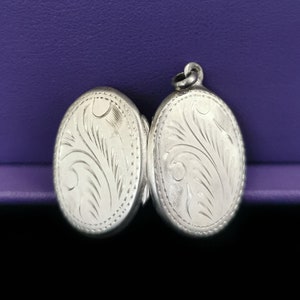 Peut inclure: Un médaillon en argent avec un motif floral gravé. Le médaillon est ouvert et les deux moitiés sont séparées.
