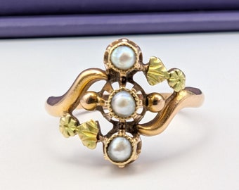 May include: A gold ring with a delicate design featuring three pearls and green accents.