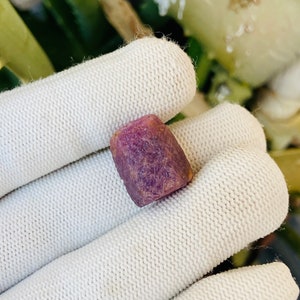 Op de afbeelding: Een diep paarse, gefacetteerde, ruwe edelsteen. De edelsteen heeft een rechthoekige vorm met afgeronde hoeken.