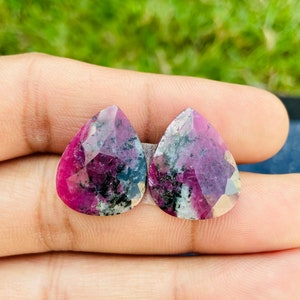 Może przedstawiać: Dwa fasetowane, błyszczące kamienie szlachetne w kształcie gruszki, w kolorze różowym, czarnym i białym.