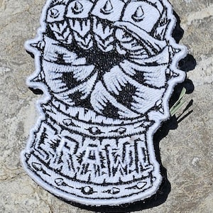 May include: A black and white embroidered patch featuring a stylized gauntlet with spiked knuckles and a wrist cuff. The word BRAWL is stitched in bold, block lettering across the base of the cuff, surrounded by a decorative border of small circles.