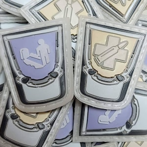 May include: A close-up of several colorful patches with different designs. The patches are made of a textured material and have a white border. The designs include a medical cross with a bullet, a person in a hospital bed, and a medical cross with a syringe.