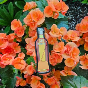 May include: A red and yellow bottle with a black cap and the text "STAMIN-UP" on the front. The bottle is surrounded by orange flowers.