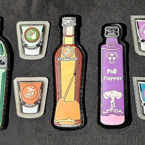 May include: Ten colorful shot glasses and bottles with various labels, including "Ginger Boo", "Speed Cola", "Pro Charger", and "Danger Zone".